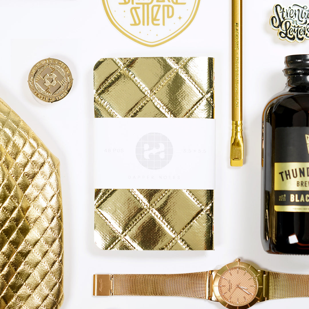 shiny gold bling pocket notebook with blackwing pencil, kenneth cole watch, and cold brew coffee