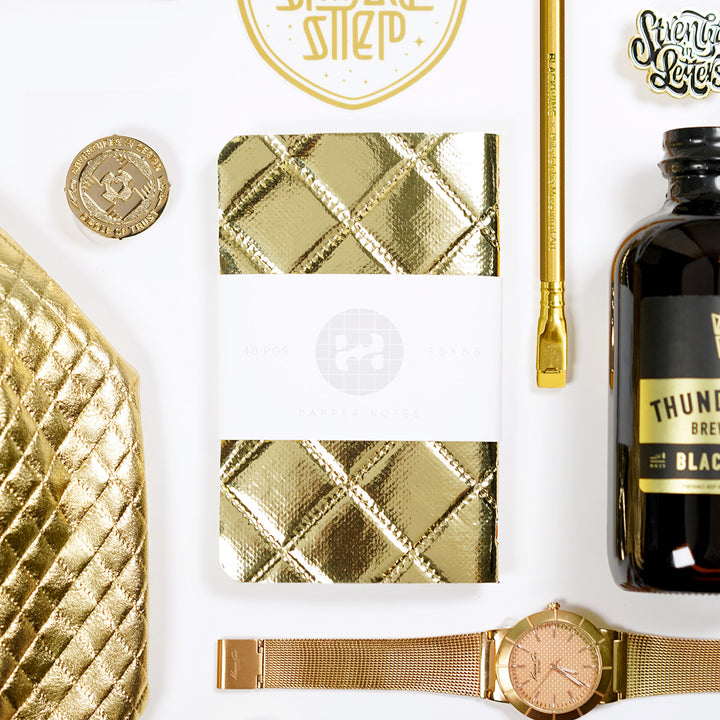 shiny gold bling pocket notebook with blackwing pencil, kenneth cole watch, and cold brew coffee