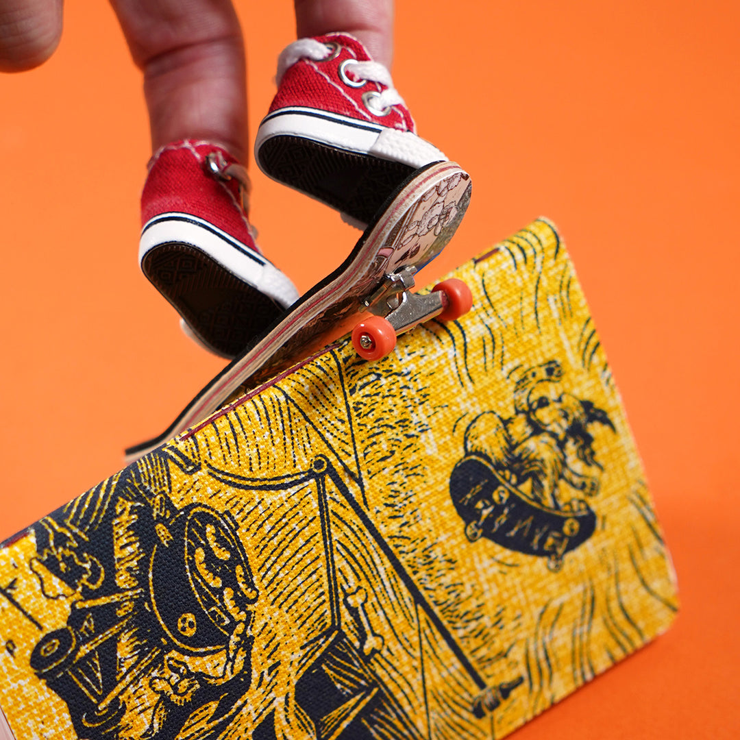 fingers inside miniature converse shoes using a tiny skateboard to jump over a yellow pocket notebook