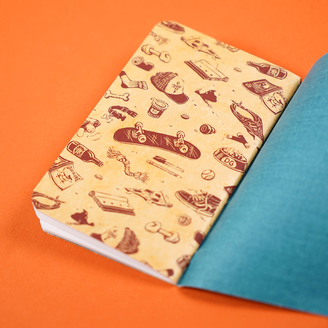 inside of a pocket notebook with a decorative endpaper featuring dog and skateboard related accessories. printing in maroon on yellow-brown paper